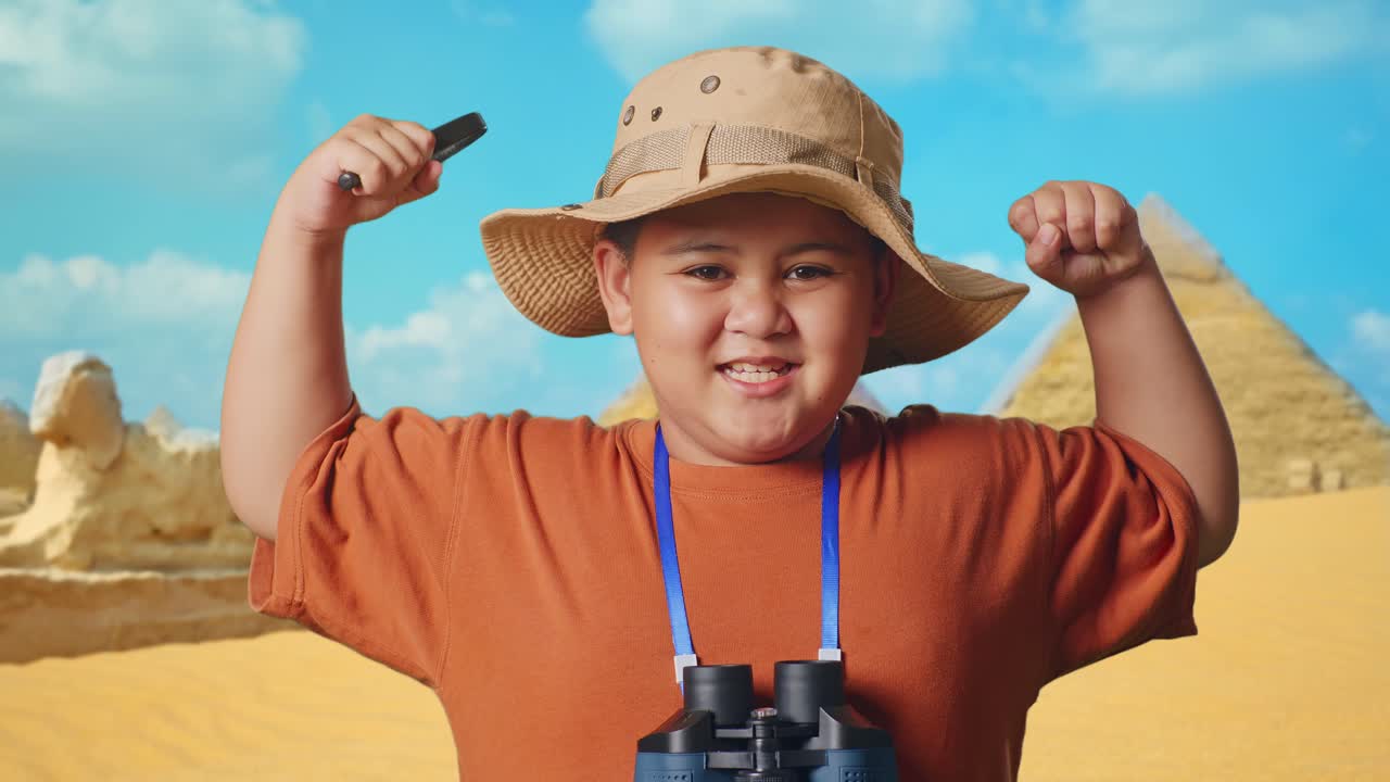 Asian Boy With A Hat And Binoculars Using The Magnifying Glass Then Flexing His Bicep While Traveling In Giza Pyramid. Boy Researcher Examines Something, Travel Tourism Adventure, Close Up