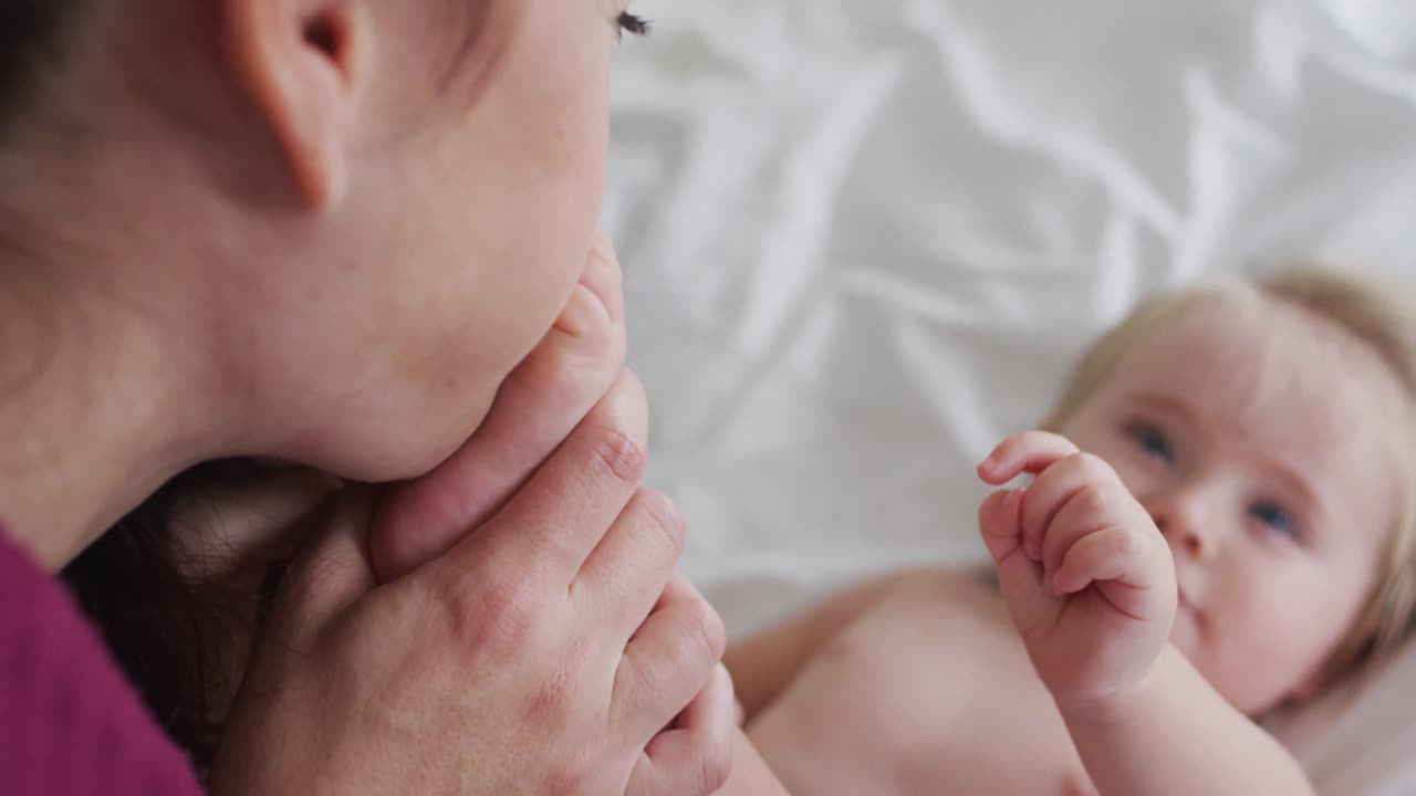 집에서 침대에서 아기의 다리를 키스하는 백인 어머니의 클로즈업