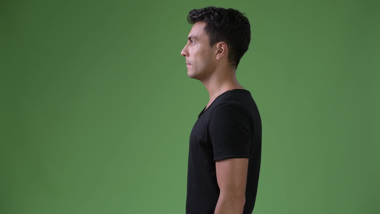 Young handsome Hispanic man against green background
