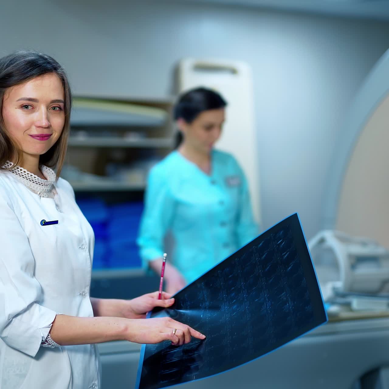 Professional female doctor with x-ray scan. Young woman in medical uniform looking at x-ray photo on the background of MRI machine in hospital.