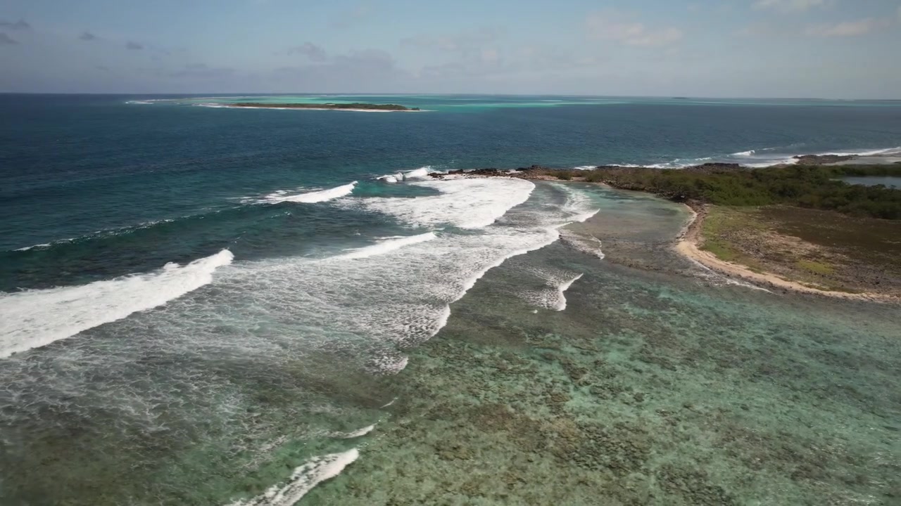 Acque cristalline, barriera corallina e costa di una piccola isola in una giornata di sole, vista aerea.