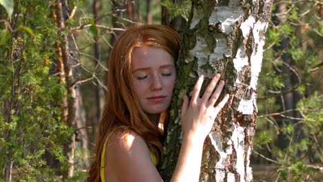 mujer joven pelirroja abrazando un árbol en el bosque