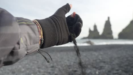 close up hand with glove, falling black sand on black sand beach in iceland