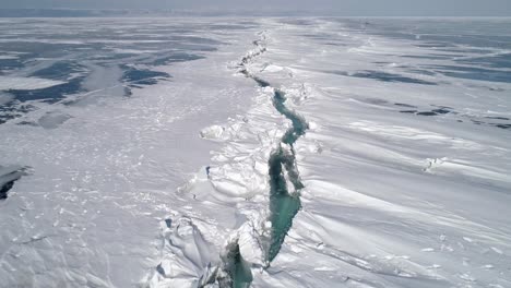 aerial above the huge deep crack on snow covered frozen ice surface of lake baikal. natural landmark. winter landscape. popular touristic destination.