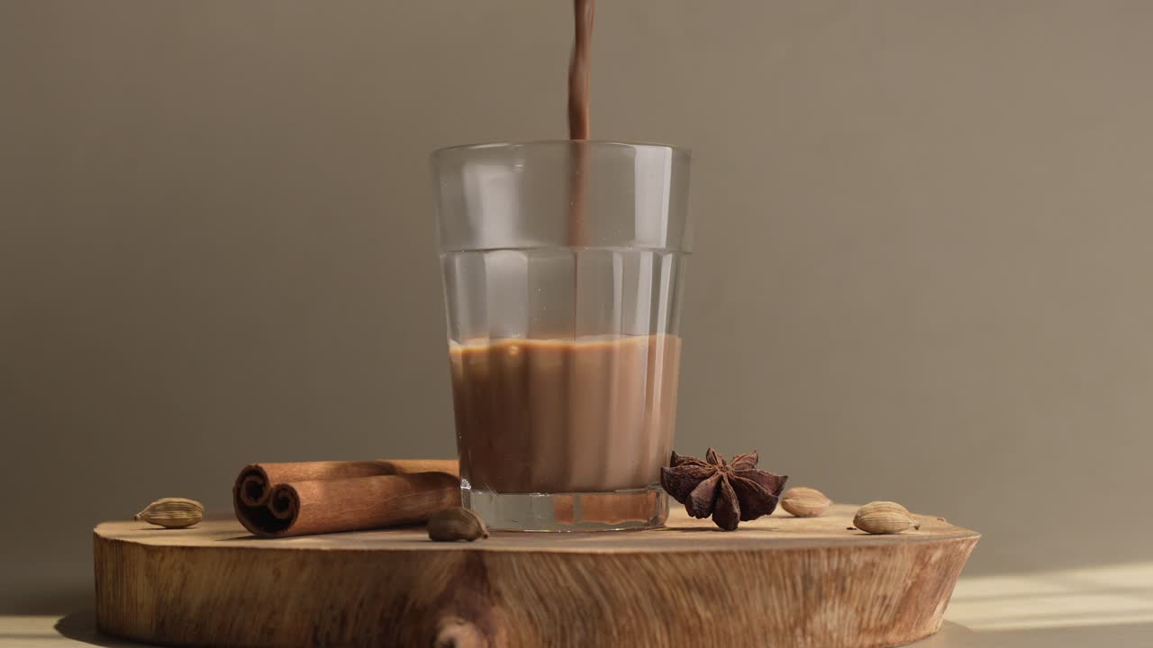 Chai indiano servito in tazze di vetro, preparato in un bollitore di metallo con masalas aromatici. Viene versato nel vetro.