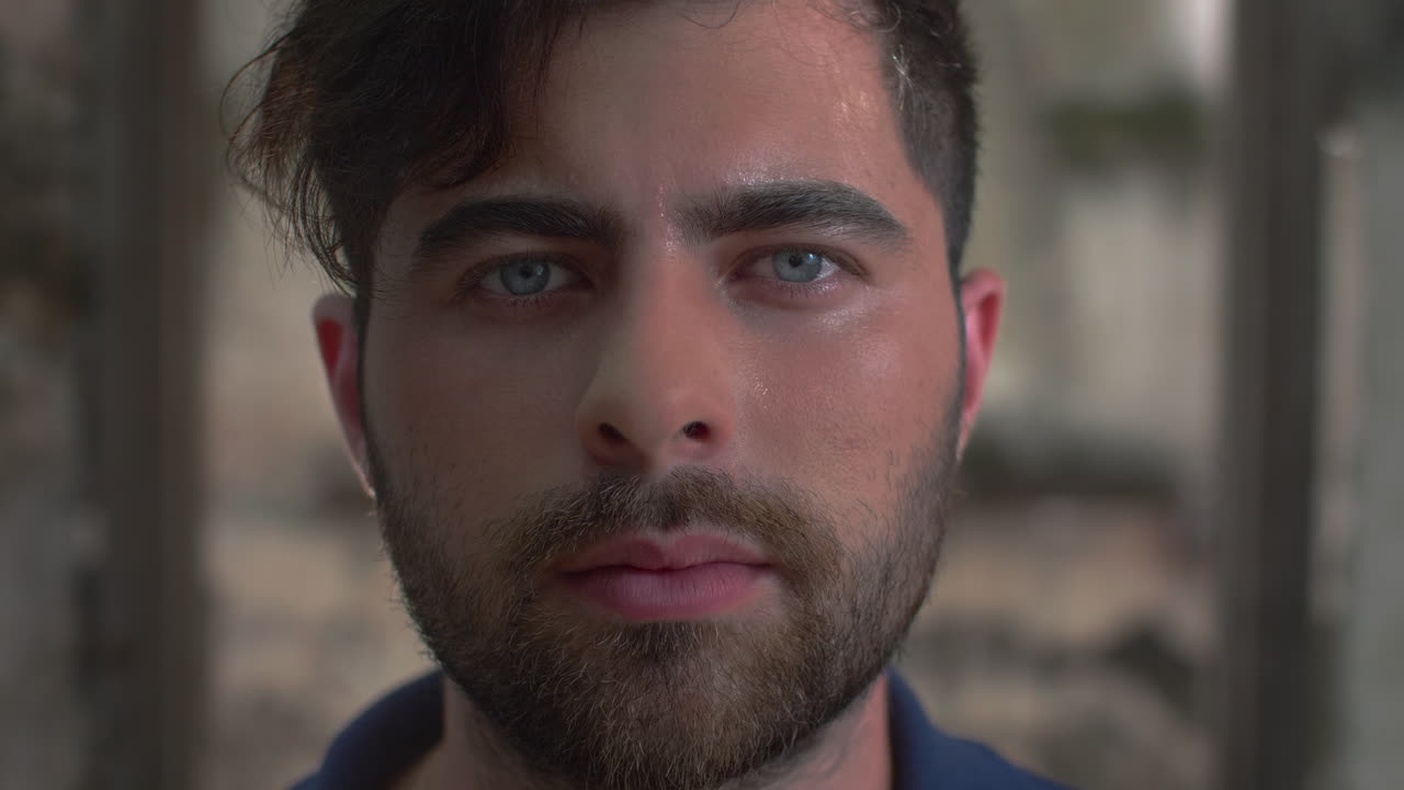 High-quality 4K footage of a focused young man with blue eyes and a beard, slowly opening his eyes in a cinematic outdoor setting. Ideal for travel, identity, mystery, or emotional
