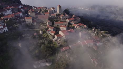 pueblo montañoso de monsanto portugal con nubes bajas al amanecer, aérea