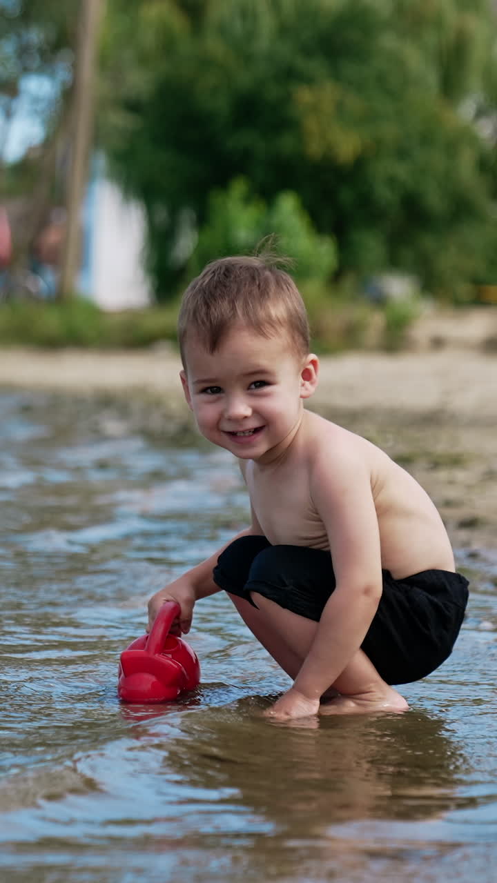 Little funny boy playing on a river beach. Water playing with splashing. Vertical video