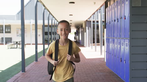 biracial boy with a backpack stands smiling in a school corridor