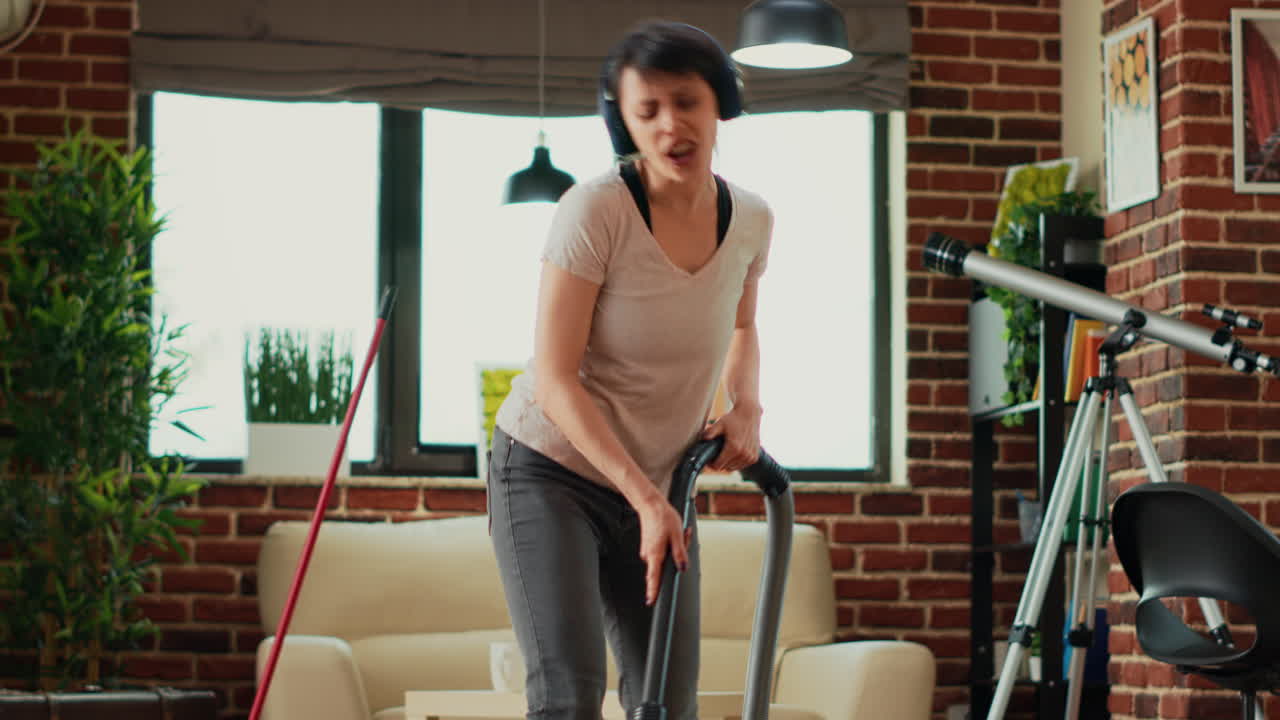 Happy housewife listening to music on headphones and vacuuming floors