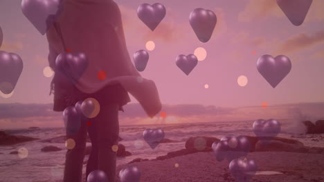 animación de corazones púrpuras sobre pareja enamorada en la orilla del mar