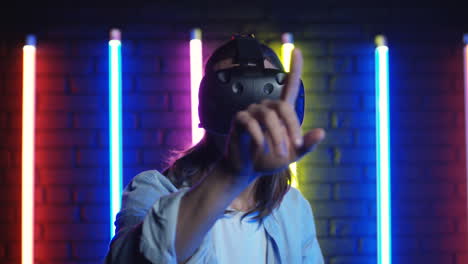 close up view of young man in vr glasses tapping and scrolling in front of him in the air in a room with colorful neon lamps on the wall