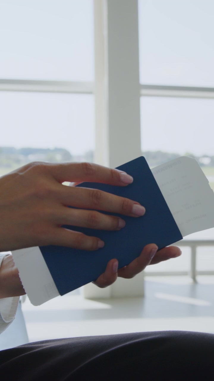 A person is reading a book at the airport with a bright window in the background vertical video