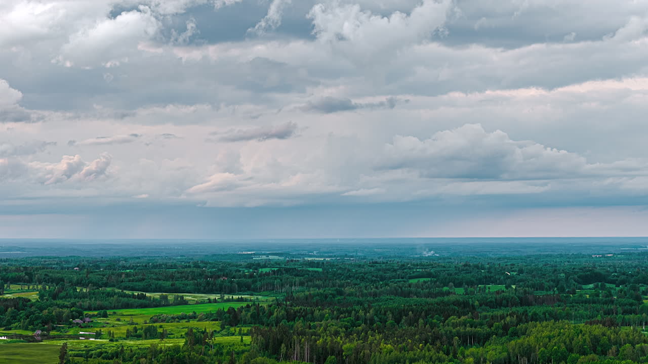 Vast landscape with low clouds over mixed green terrain, stretching toward the horizon, static timelapse backdrop