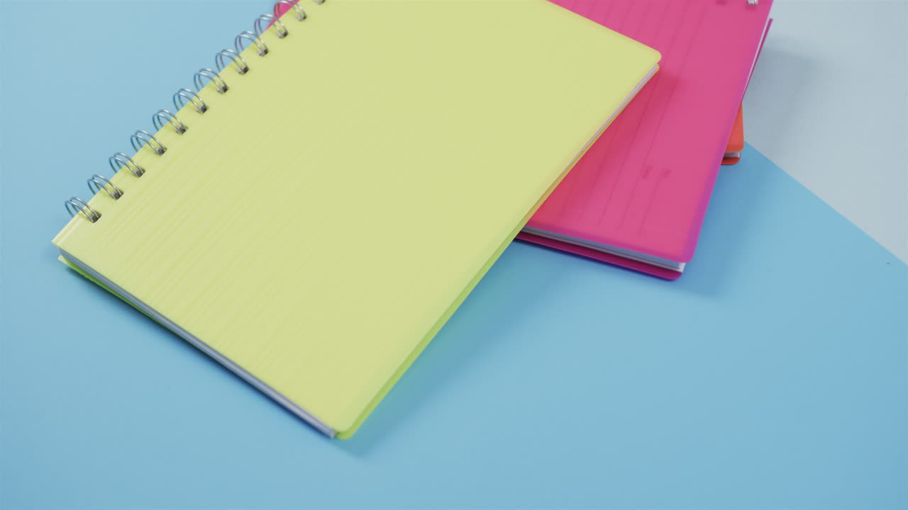 cuadernos en espiral amarillos y rosados se superponen sobre un fondo azul, con espacio para copiar