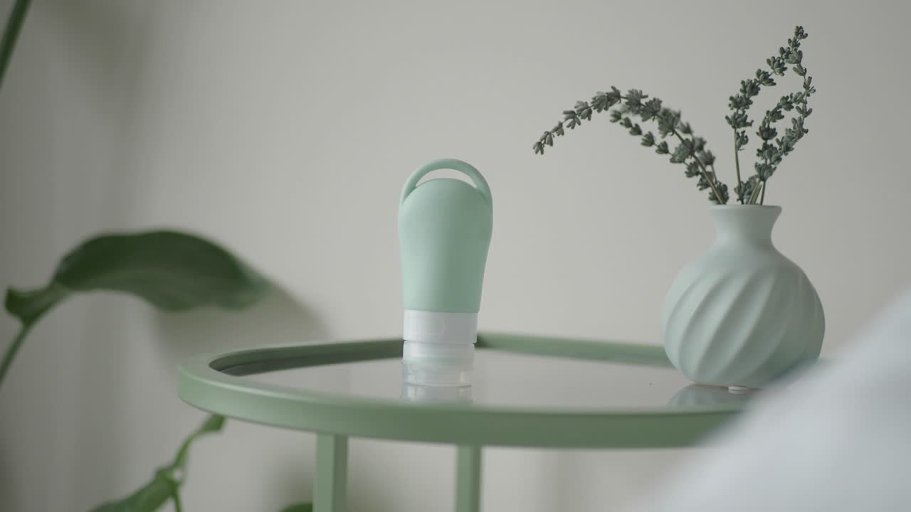 Bouteille de voyage en silicone verte et vase de lavande sur table d'appoint.