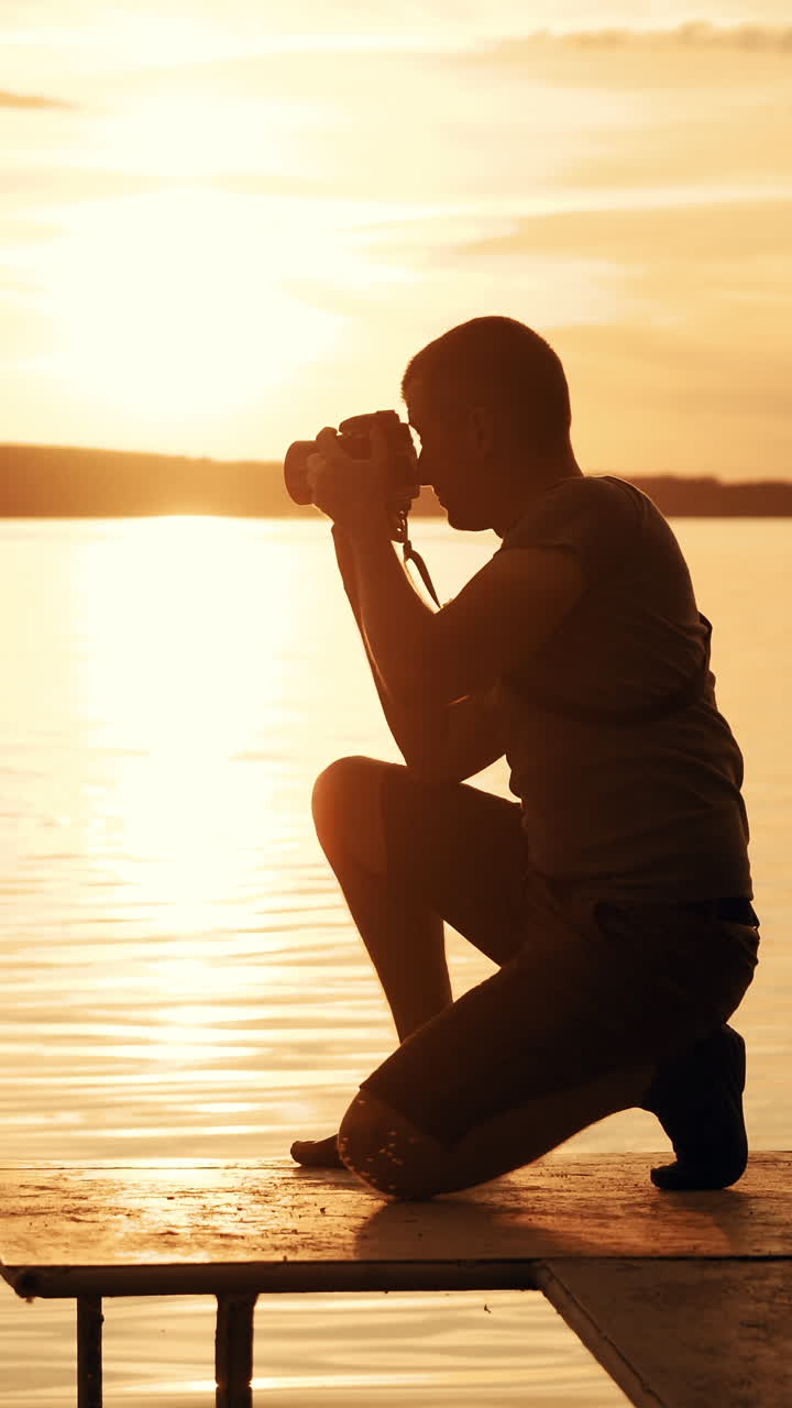 Photographer taking picture of landscape during sunset. Silhouette of people swimming in the river at sunset. Vertical video