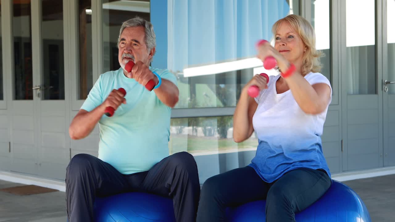 pareja de ancianos haciendo ejercicio con mancuernas en una pelota de ejercicio