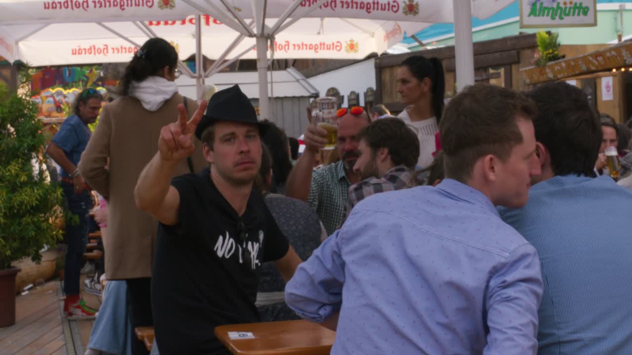 Crowd of people sitting and drinking beer while happily waving at Balvarian outdoor Spring Fest in Stuttgart, Baden Wurttemberg, Germany, Europe, afternoon panning view angle