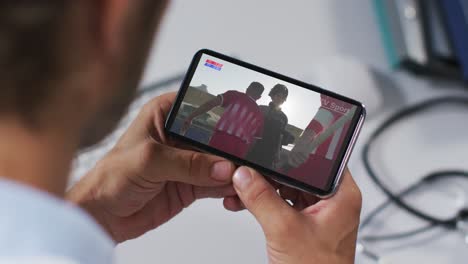 compuesto de un médico masculino viendo un evento deportivo en un teléfono inteligente