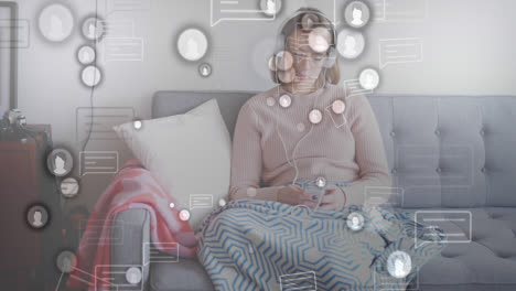 animation of social media icons over caucasian woman wearing headphones using smartphone at home