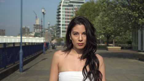 attractive and playful hispanic latina woman walking towards the camera, on the riverbank of the thames in london, uk