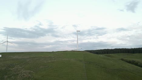 Low-aerial-approaches-wind-turbine-being-erected-on-pasture-hilltop