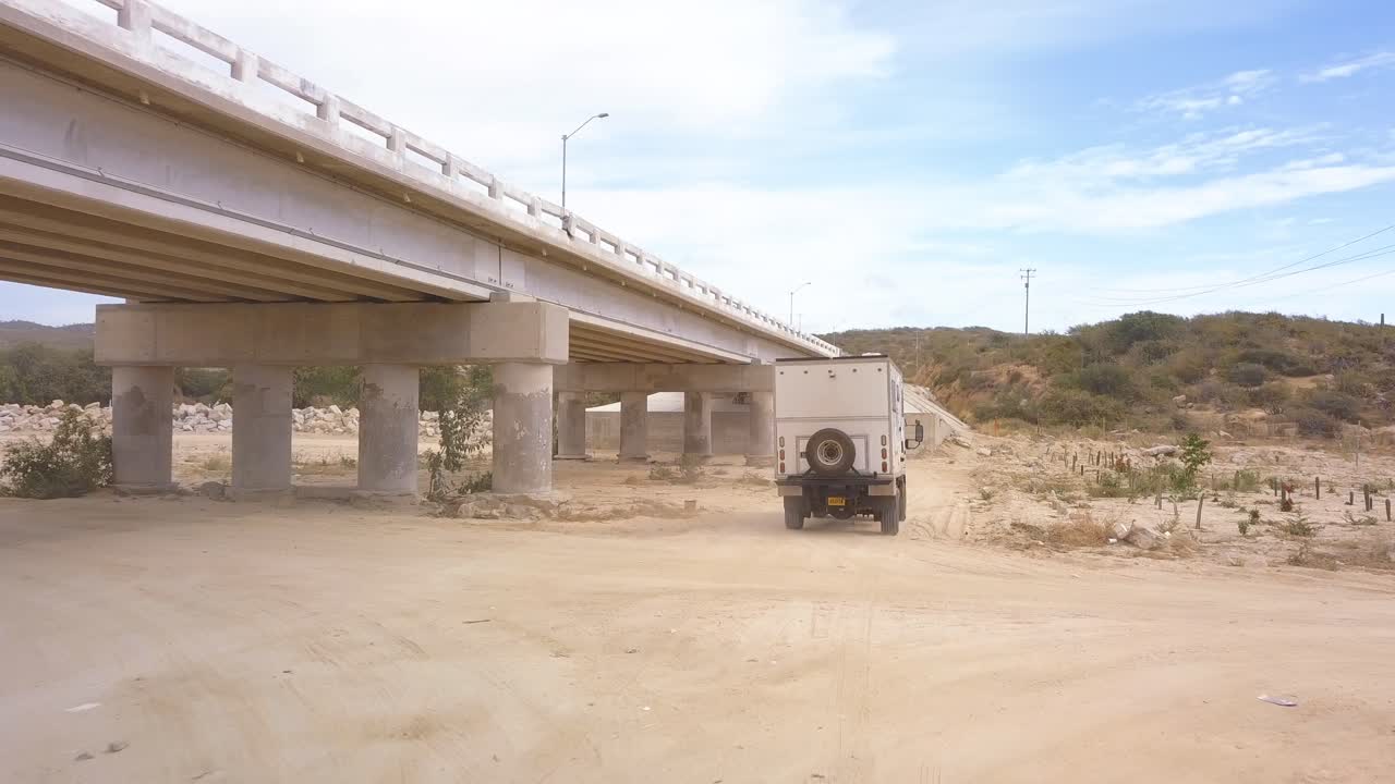 Low aerial shot following a motor home driving under a highway in Baja California.