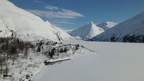 Aerial-View-of-Lake-and-Mountains-Covered-in-Snow-with-blue-sky-and-clouds