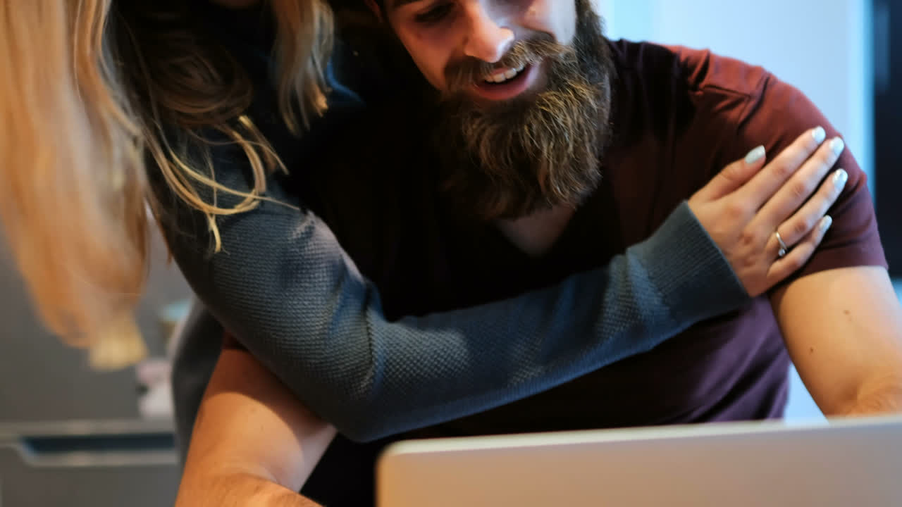 Couple embracing each other while using laptop at home 4k