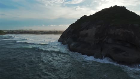 Wellen,-Die-Gegen-Die-Schroffen-Klippen-Krachen,-Mit-Dem-Strand-Im-Hintergrund