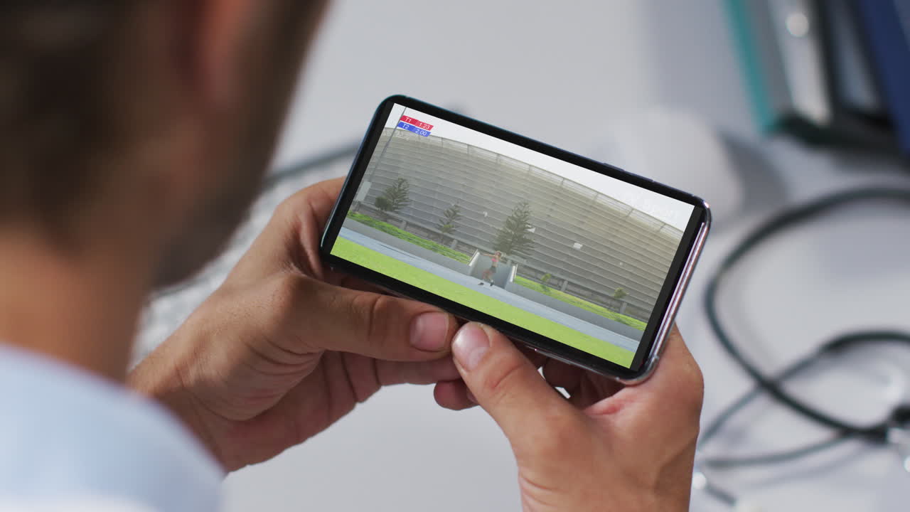 compuesto de un médico masculino viendo un evento de jabalina de atletismo en un teléfono inteligente
