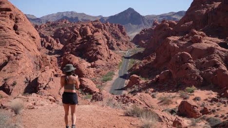 young woman with photo camera on viewpoint above desert road in valley of fire, state park in nevada usa, back view, full frame slow motion