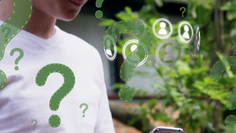 signo de pregunta e iconos de perfil flotando contra un niño caucásico usando un teléfono inteligente en el jardín