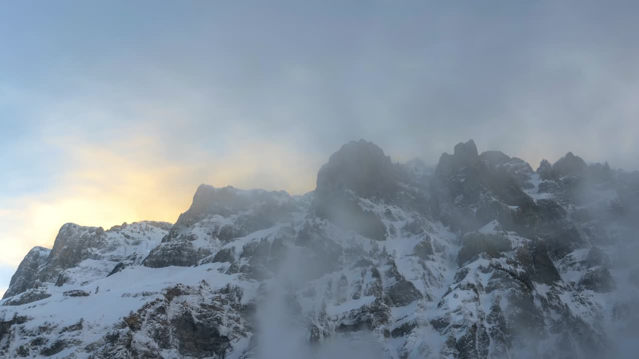 산맥 뒤에 겨울에 해가 지면, 눈은 강한 바람에 의해 어지고 지평선의 하늘은 노란색으로 빛납니다. 안개와 바람이 있습니다. 크리스마스에 아름다운 풍경.