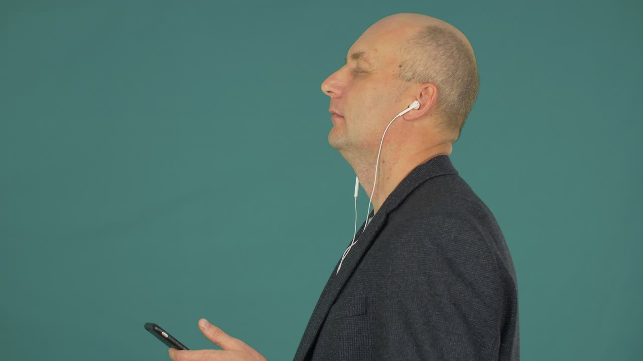 Handsome man listening music in headphones by mobile phone and dancing on green background. Side view.