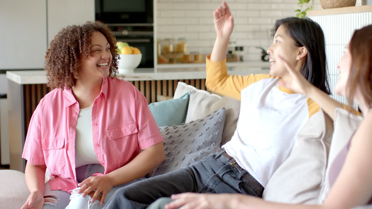 Laughing and chatting, three diverse women friends enjoying time together on couch at home