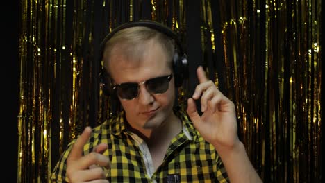 portrait of caucasian man dancing on black background. gold shining foil strips. party, music, disco