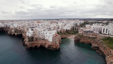 Aerial-orbit-view-of-Polignano-a-mare-town-on-rugged-coastline-in-Puglia,-Italy