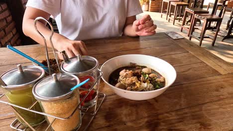 person adding various condiments to noodle soup