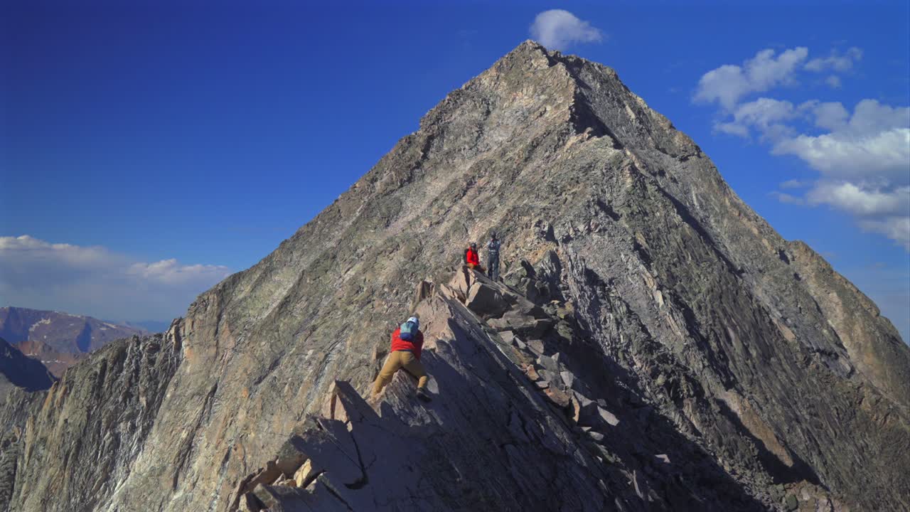 Knifes Edge Trail Capitol Peak north east ridge Wilderness Hikers scrambling rock climbing Rocky Mountains Colorado 14er mountainside large boulders aerial view summer blue sky morning sunny clouds