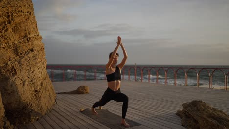 woman practicing yoga by the sea at sunset