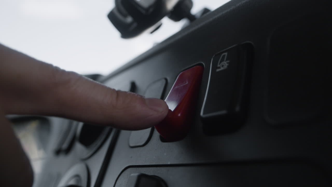 Finger pressing red hazard light button in a car