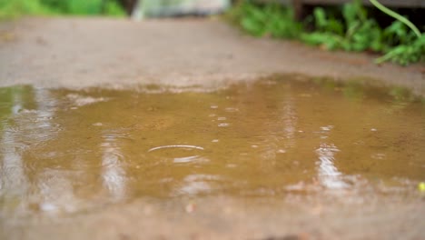 Regentropfen-Regnen-In-Zeitlupe-In-Eine-Pfütze-Auf-Einer-Sandigen-Straße