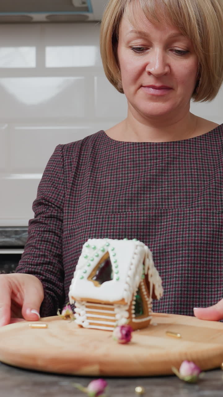 체크 로 된 드레스 를 입은 여자 는 조심스럽게 회전 하는 동안 컵 을 내려 놓습니다. 나무 트레이 에 장식 된 생강  집, 불, 쿠키 및 녹색 구슬 을 가진 아 한 부 설정