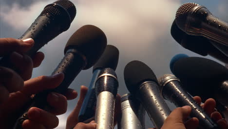 multiple microphones held by hands at an outdoor event, covered in raindrops