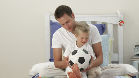 Father-and-son-playing-with-a-soccer-ball-in-bedroom