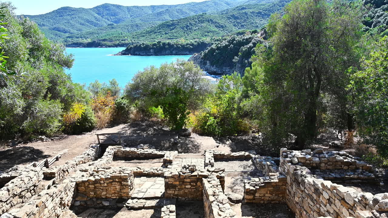 Ancient construction excavations on a hill with greenery around, Aegean sea coast on the background in Greece