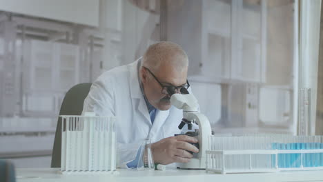 Bearded-Caucasian-male-researcher-wearing-protective-glasses-and-working-with-a-microscope-spbas.-scientist-using-microscope-in-a-laboratory.-Search-for-coronavirus-vaccine.-High-quality-4k-footage