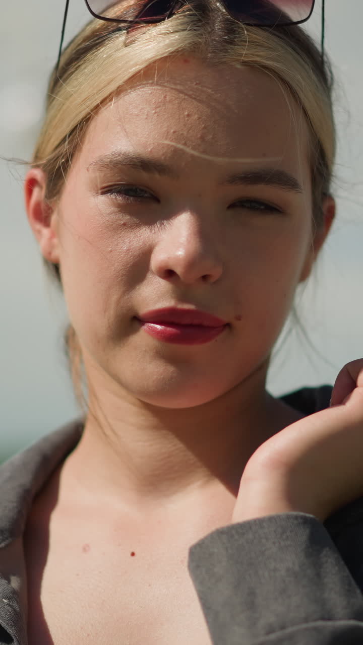 회색 셔츠와 머리에 선글라스를 입은 백인 여성은 그녀의 어깨에 다채로운 쇼핑 가방을 들고, 집중된 표정으로, 배경에 흐릿한 전기 기둥을 가지고 있습니다.